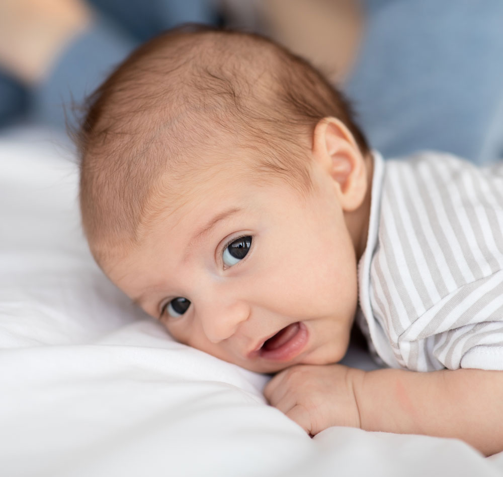 Baby lying alert on tummy on bed