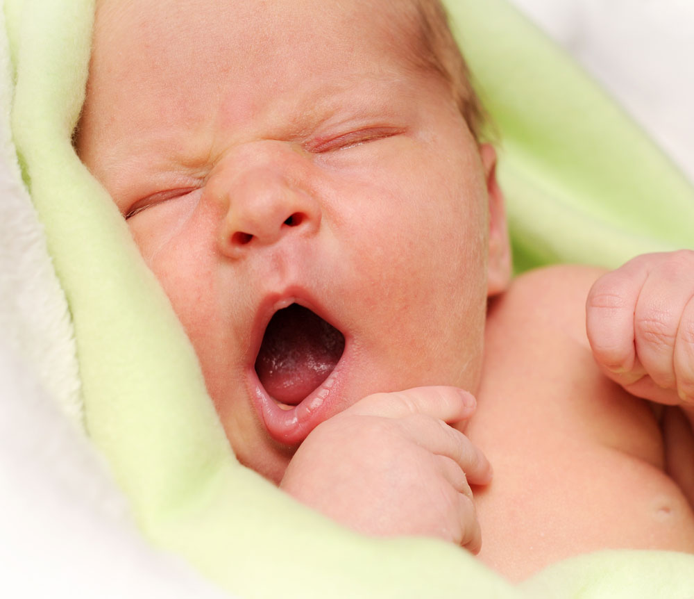 Newborn baby yawning in green blanket
