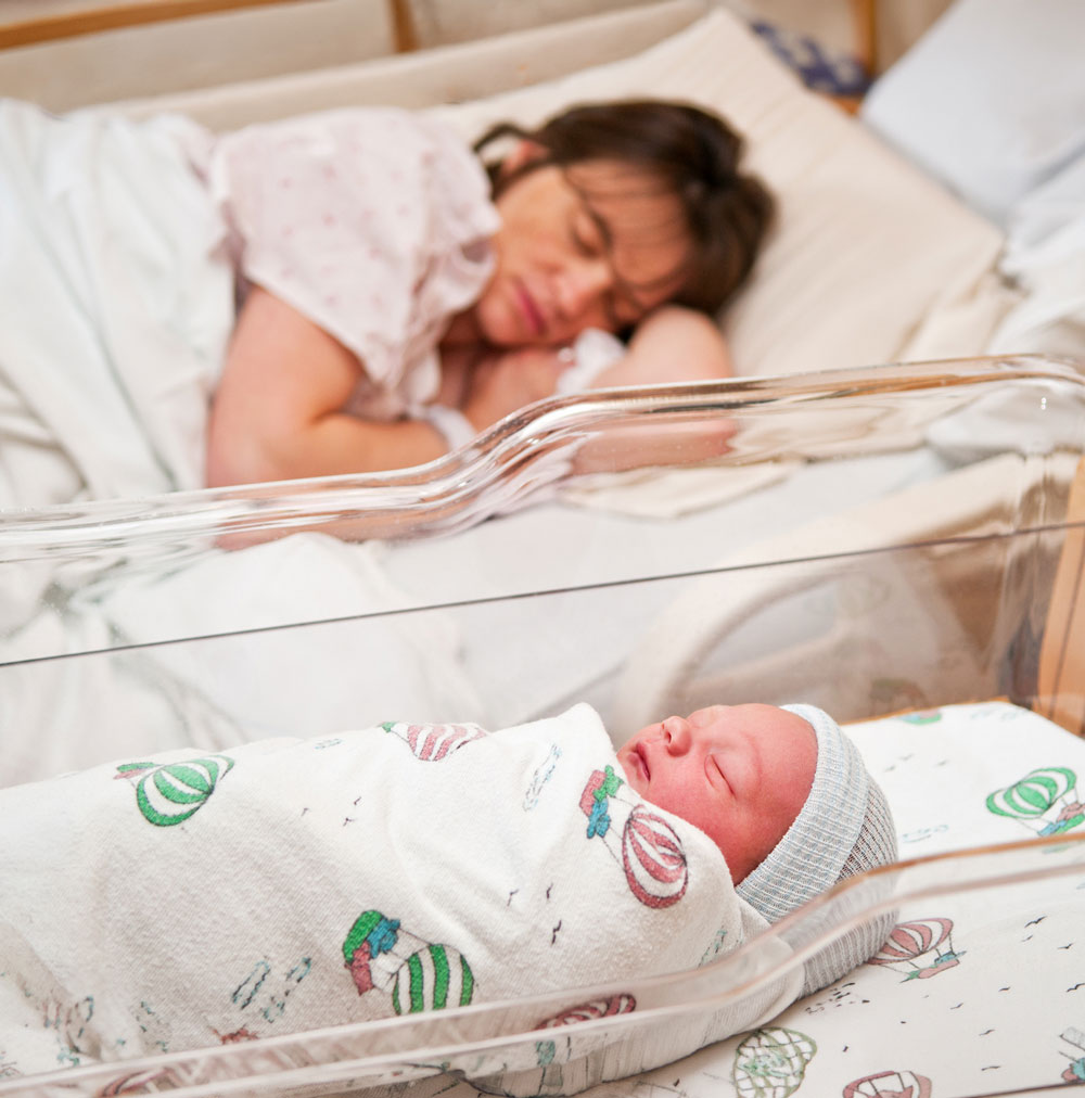 Newborn in bassinet, mother resting nearby