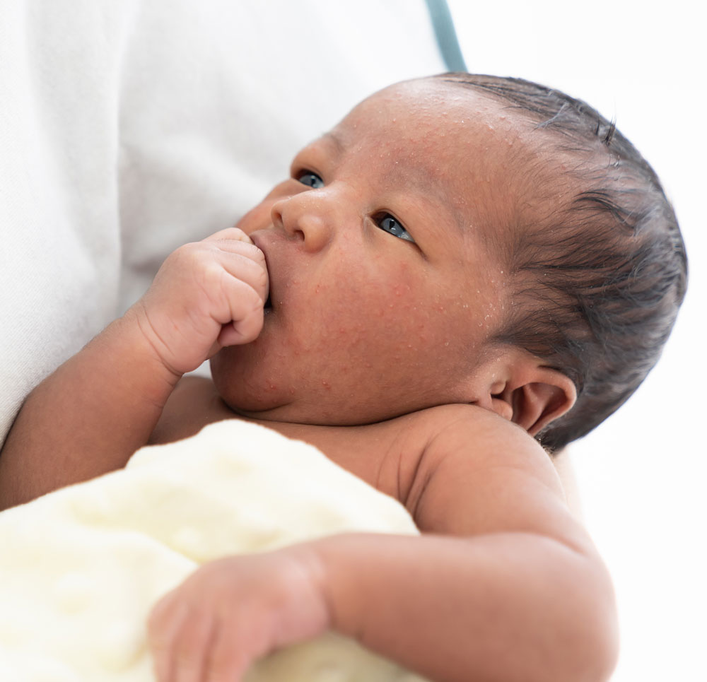 Newborn resting on shoulder, hand near mouth