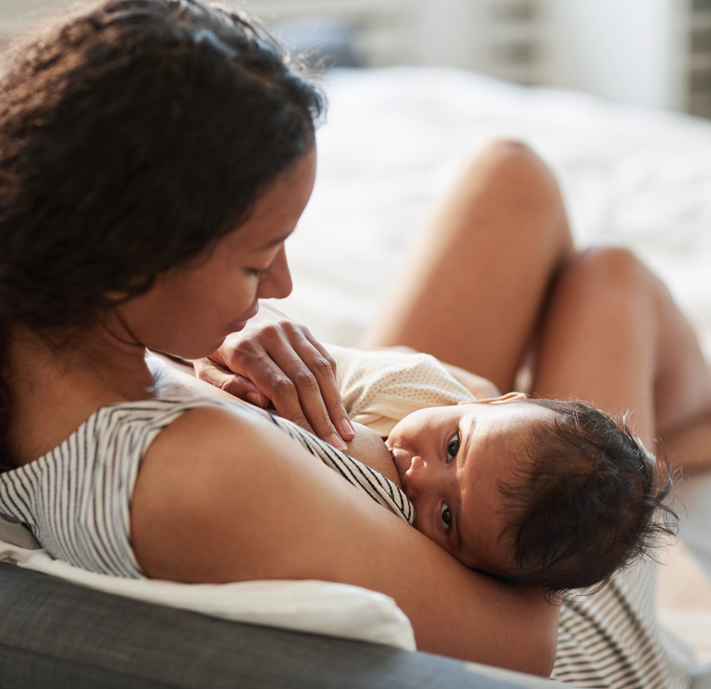 mother gently breastfeeding her infant on a bed