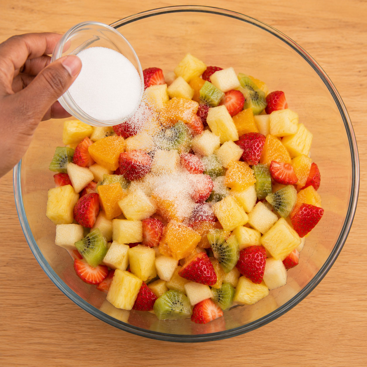 Hand sprinkling sugar onto mixed fruit salad bowl