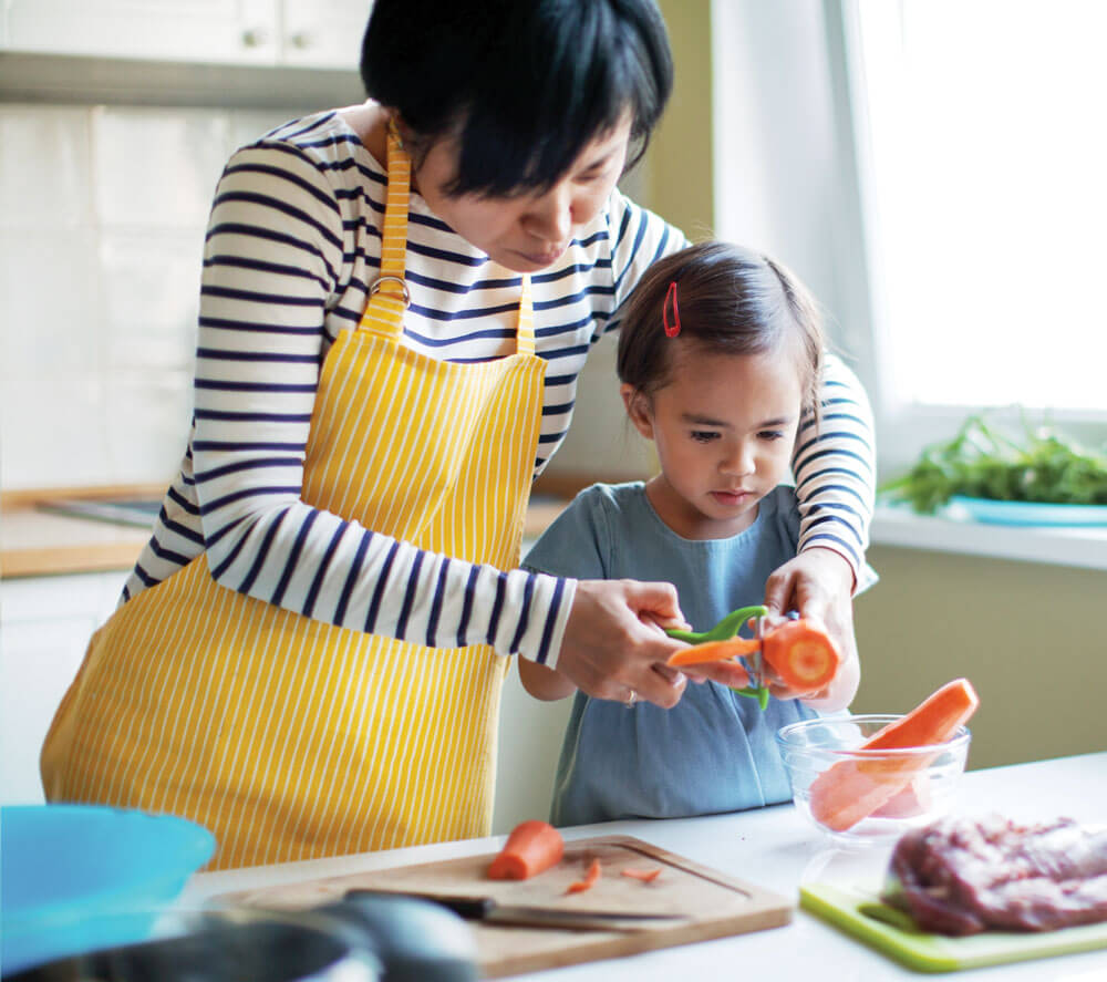 A young girl helping her mother in the kitchen with food preparation.