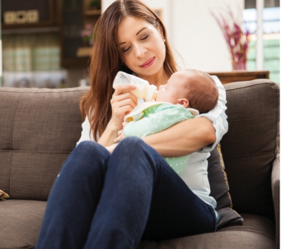 The baby, dressed in a light-colored outfit, gazes back comfortably in her arms.