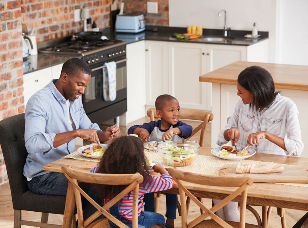 Photo of a smiling family, consisting of a mother, father, and two children, enjoying a moment together outdoors.