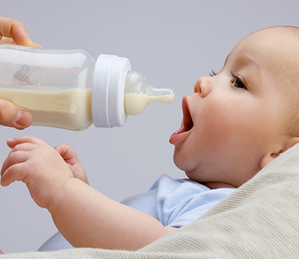 A caregiver practicing paced bottle feeding, holding a baby in an upright position while gently offering a bottle.