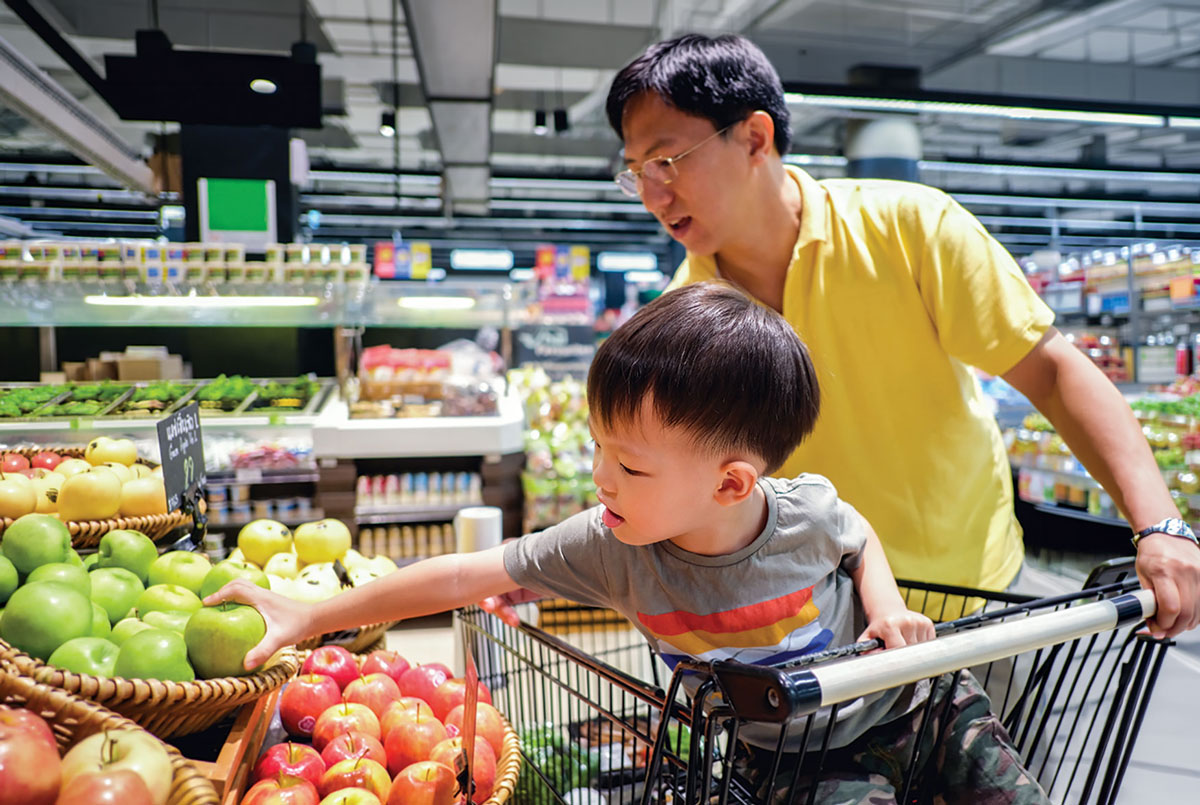 Child reaching for apples in grocery store cart.
